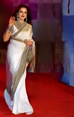 a woman in a white sari walking on a red carpet with her hand up