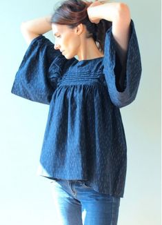 a woman standing in front of a white wall with her hands on her head, wearing jeans and a blue top