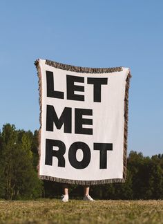 a person holding a sign that says let me rot in front of some trees and grass