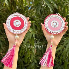 two hands are holding small red and pink objects with tassels on them,