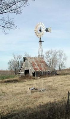 an old barn and windmill in the middle of a field with no leaves on it