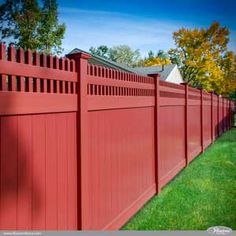 a red fence with green grass and trees in the back ground, behind it is a house