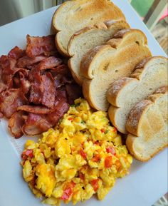 scrambled eggs, toast and bacon on a white plate next to some slices of bread