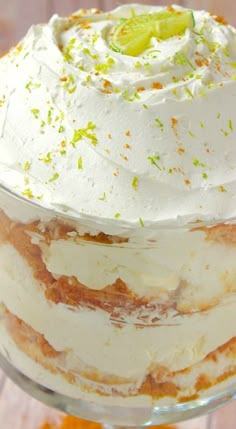 a layered cake with white frosting and limes on top is sitting in a glass dish