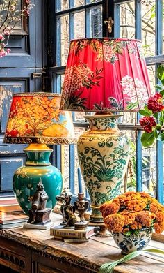 vases with flowers are sitting on a table in front of a window and lamp