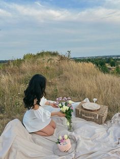 a woman sitting on top of a blanket next to a basket with flowers in it