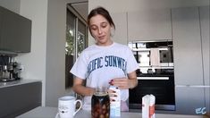 a woman standing in a kitchen with jars and cups on the counter next to her