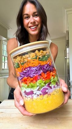 a woman holding up a large jar filled with different types of vegetables and meats