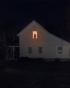 a white house at night with the light on and windows lit up in the dark