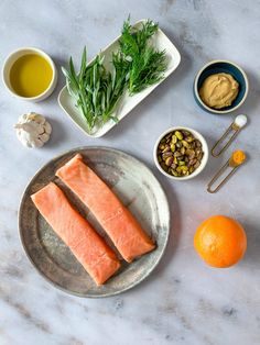 two salmon fillets on a plate next to other ingredients and an orange, some with green garnishes