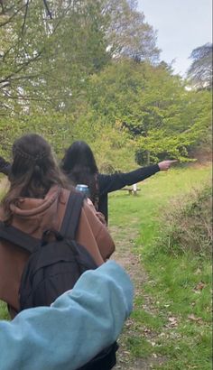 two women pointing at something in the distance on a grassy area with trees and grass