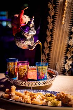 a person pouring tea into some cups on a tray with other items in front of them