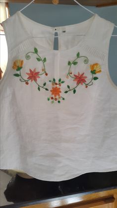 a white top with flowers on it hanging from a rack