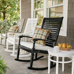 three rocking chairs sitting on the front porch with pillows and throw pillows, next to a small table