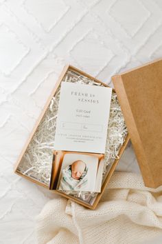 an open box with photos inside on top of a white blanket next to a pillow