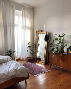 a bedroom with a bed, mirror and plants on the wall next to it's windows