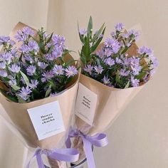 two bouquets of flowers wrapped in brown paper and tied with purple ribbon, sitting on a table