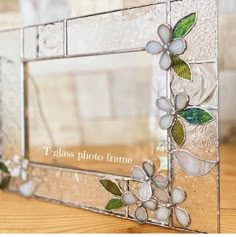 a decorative glass frame with flowers and leaves painted on the side, sitting on a wooden table