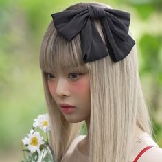 a girl with long blonde hair wearing a black bow and holding a bouquet of daisies