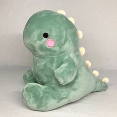 a green dinosaur stuffed animal sitting on the ground