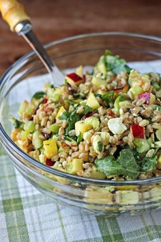 a glass bowl filled with salad on top of a green and white table cloth next to a wooden spoon