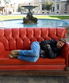 a man laying on top of a red couch next to a fountain