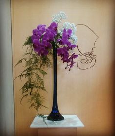 purple and white flowers are in a black vase on a small table next to a wall