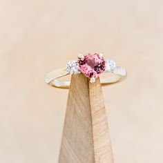 a pink diamond ring sitting on top of a wooden stand