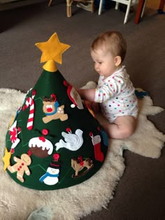 a baby is sitting on the floor next to a christmas tree shaped like a cone