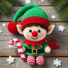 a crocheted christmas elf doll sitting next to a candy cane on a wooden table