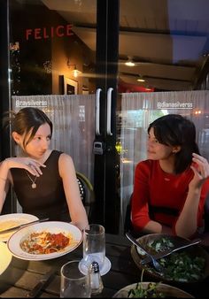 two women sitting at a table with plates of food