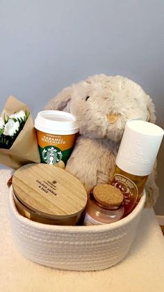 a stuffed animal is sitting in a basket with coffee and other items on the table