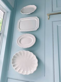 three white plates are hanging on the wall next to a window in a blue room