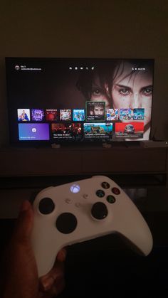 a person holding a white controller in front of a flat screen tv with movies on it