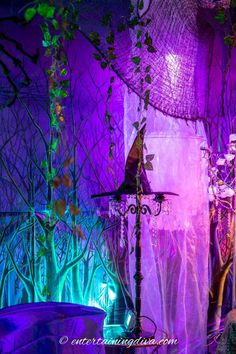 a purple and green halloween display in a room with trees on the wall, witch's hat hanging from a lamp post