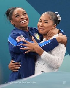 two women hugging each other in front of a blue wall with an american flag on it