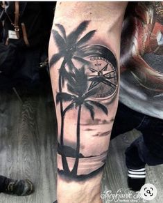 a man's arm with a palm tree and compass tattoo on the left forearm