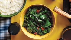 a bowl filled with green vegetables next to rice and other foods on a yellow table