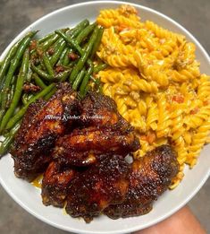 a plate with meat, pasta and green beans on it is being held by someone's hand