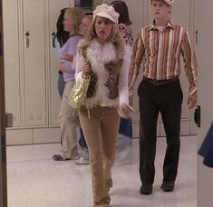 two people walking down a hallway in front of lockers with one person wearing a hat and the other holding a purse