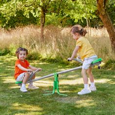 two young children playing on a sees - vert in the grass near some trees