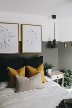 two framed pictures hang on the wall above a bed with white sheets and yellow pillows