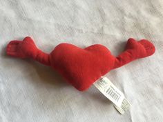 a red heart shaped stuffed animal laying on top of a white sheet with a tag attached to it