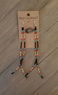 a pair of beaded earrings on top of a wooden table next to a card