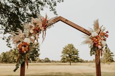 an arch decorated with flowers and feathers is set up in the middle of a field