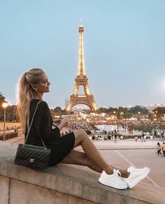 a woman sitting on a ledge in front of the eiffel tower