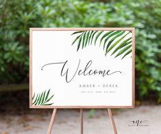 a welcome sign with palm leaves on it in front of some bushes and greenery