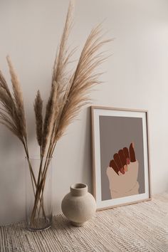 a vase with some dry grass in it next to a framed print on the wall