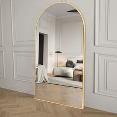 a large mirror sitting on top of a wooden floor next to a white bed in a room