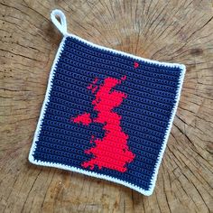 a crocheted red and blue square with the shape of britain on it sitting on top of a wooden table